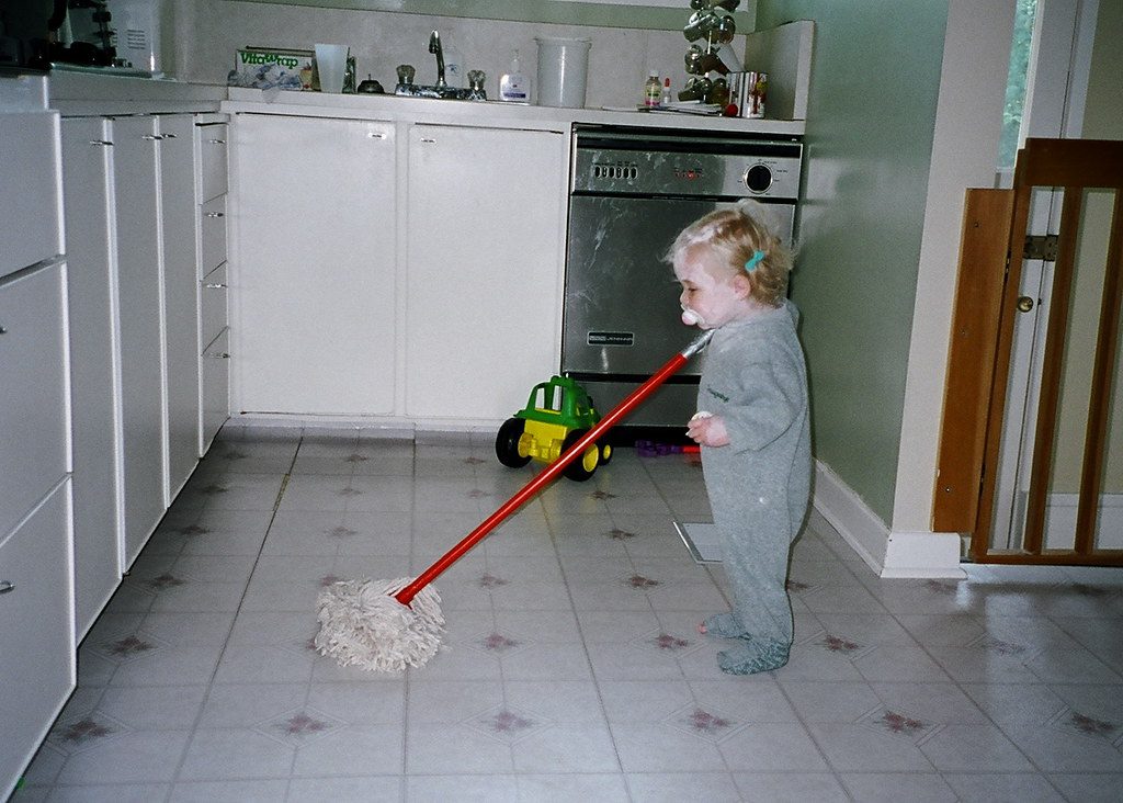 Child holding mop in kitchen